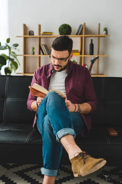 戴眼镜的年轻男性坐在皮革沙发和读书书上 — 图库照片
