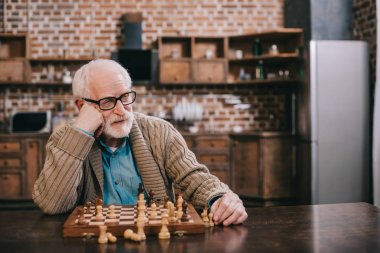 Bored senior man playing chess clipart