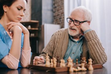 Thoughtful nurse and elder man playing chess clipart