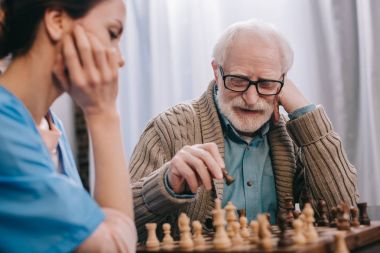 Senior man enjoying playing chess with nurse clipart