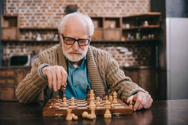 Clever senior man playing chess alone