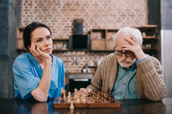 Gelangweilte Krankenschwester Und Älterer Mann Beim Schachspielen — Stockfoto