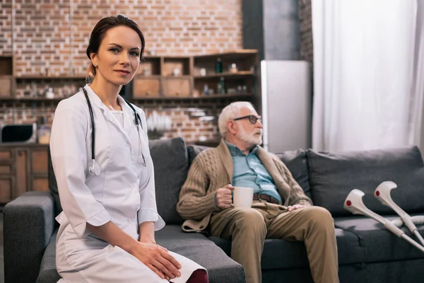 ソファの上の年配の男性で座っている白衣の女医 — ストック写真