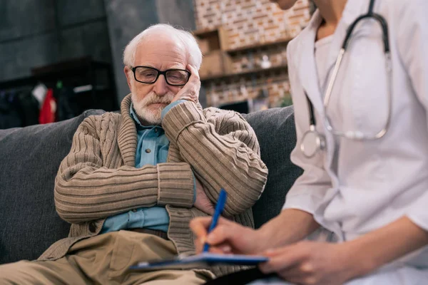 Trauriger Senior Schaut Arzt Der Medizinische Beschwerden Aufschreibt — Stockfoto