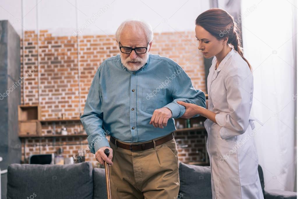 Doctor helping elder male patient with cane