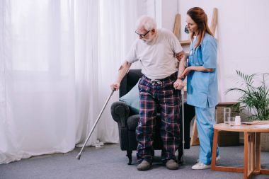 Nurse helping male patient with crutches clipart