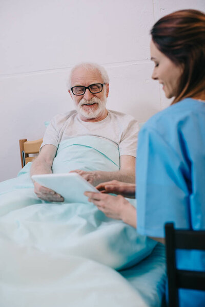Senior patient in bed and nurse using tablet