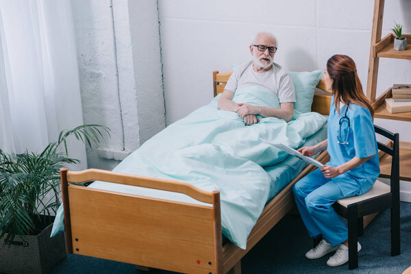 Old man patient and nurse discussing news from newspaper