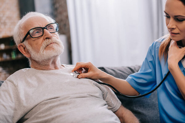 Nurse with stethoscope checking heartbeat of senior man