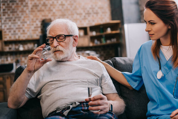 Nurse sitting by senior man taking medications