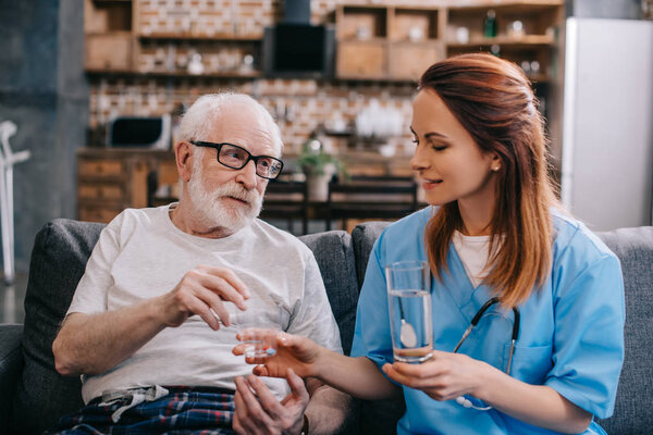 Nurse giving a glass of water to patient with pills
