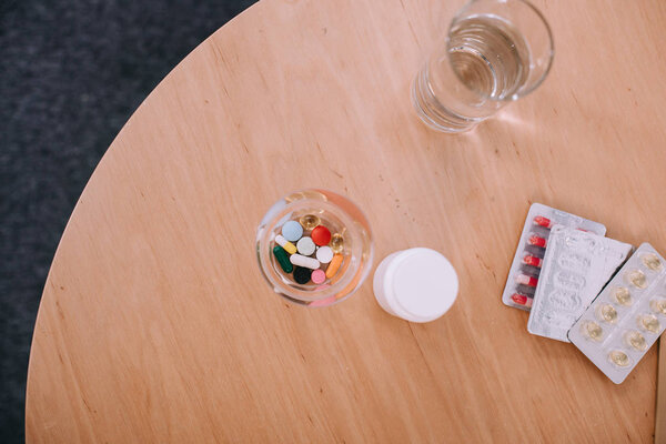 Different colorful pills and capsules with glass of water on table