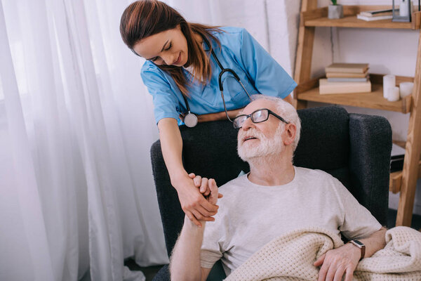 Nurse supporting and holding hand of smiling senior man patient