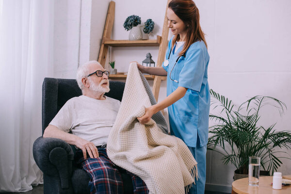 Nurse covering senior patient with plaid
