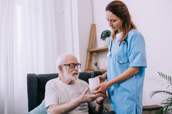 Nurse helping senior patient to hold a cup