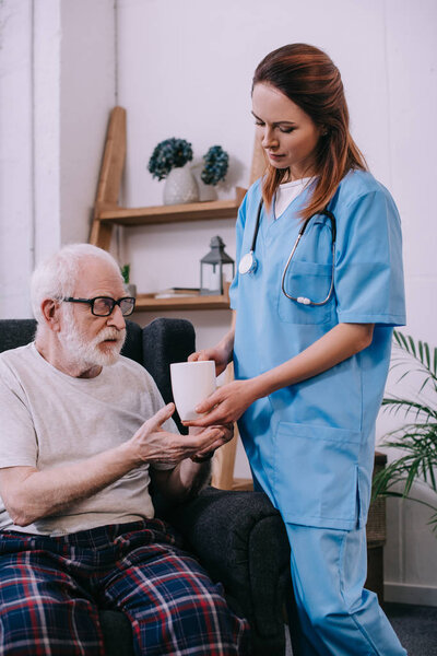 Nurse giving cup with drink to senior patient 