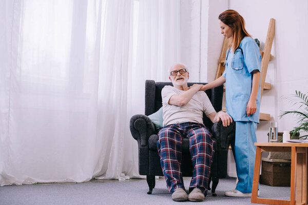 Female caregiver supporting senior man patient