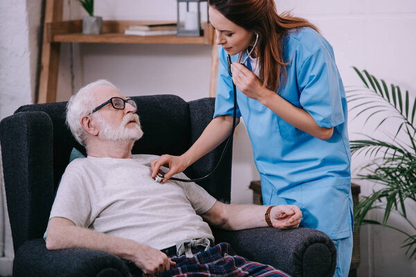 Nurse with stethoscope checking heart rate of senior patient