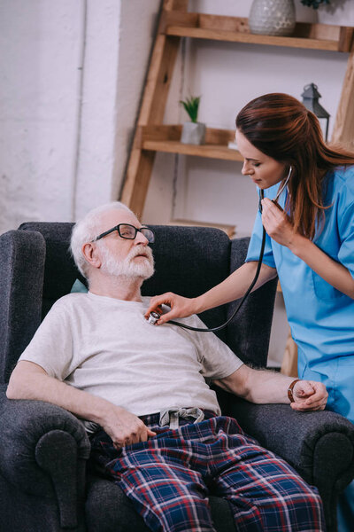 Nurse with stethoscope checking heartbeat of senior man
