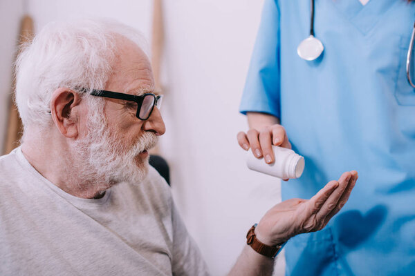 Female nurse giving pills to senior patient