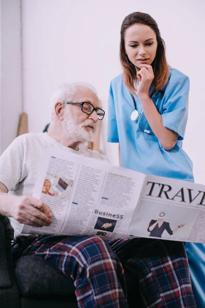 Nurse Standing Senior Man Reading Newspaper — Stock Photo, Image