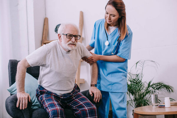 Nurse helping old man to stand up from chair