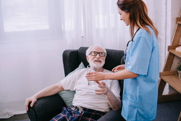 Nurse giving a glass of water to senior patient 