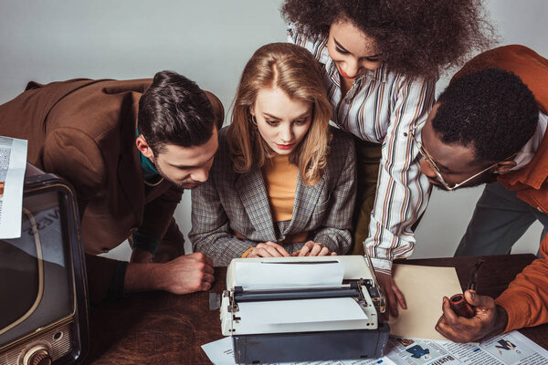 multicultural retro styled journalists looking at text at typewriter