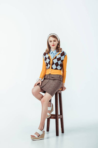 attractive retro styled girl sitting on wooden chair and looking at camera on white