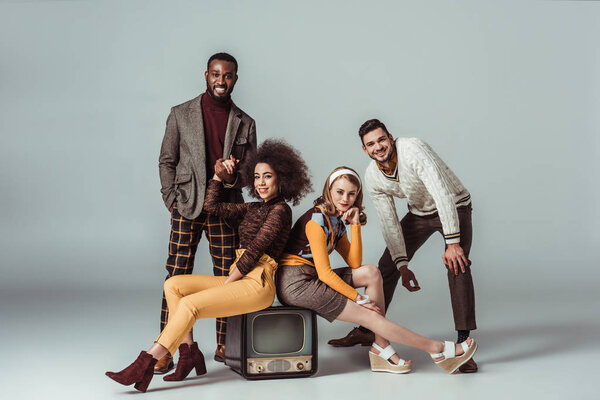 multicultural retro styled friends posing with vintage television on grey
