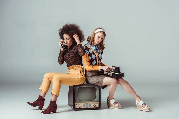 мультикультурные девушки в стиле ретро сидят на старом телевизоре и разговаривают по стационарному телефону
