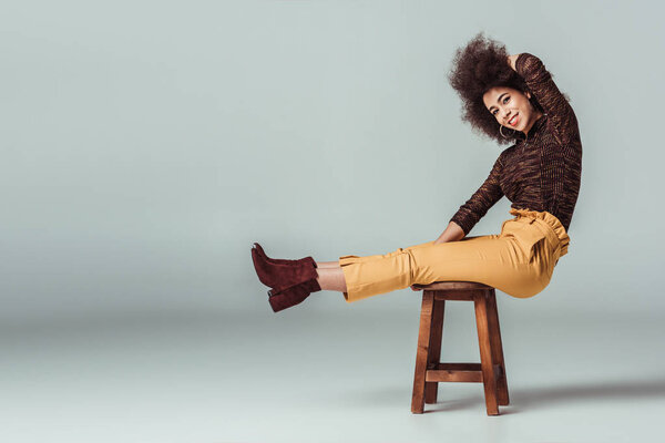 side view of african american woman in retro clothes sitting on chair on grey