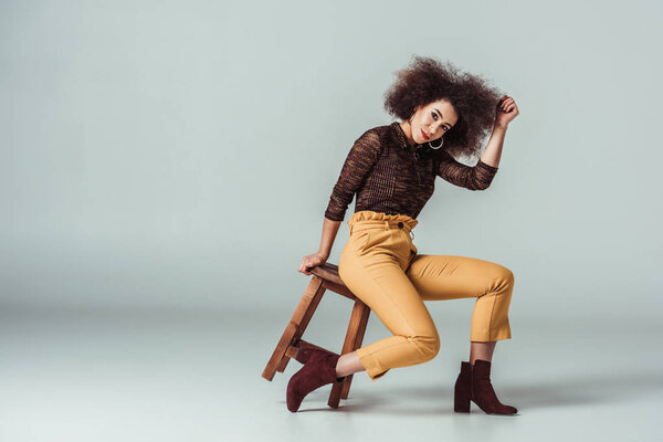 african american woman in retro clothes posing on chair on grey