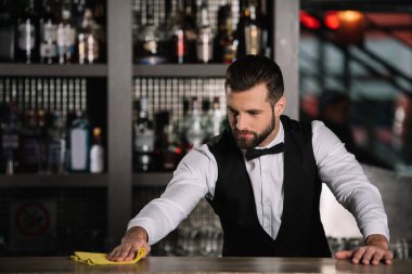 handsome bartender cleaning bar counter in evening clipart