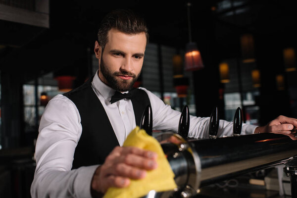 handsome bartender cleaning beer taps in evening