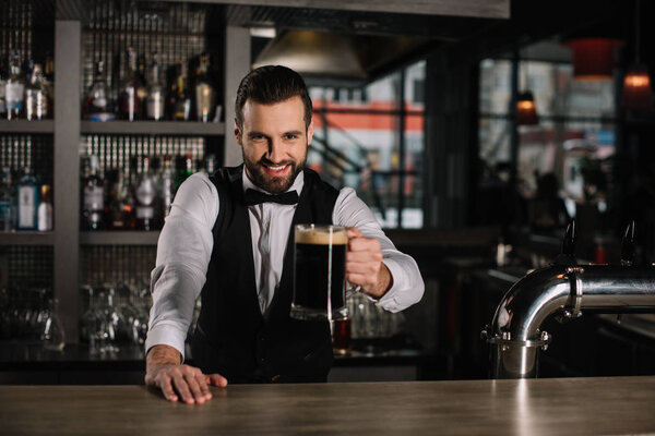 smiling handsome bartender holding glass of beer