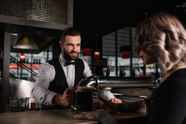 smiling handsome bartender giving glass of beer to female visitor