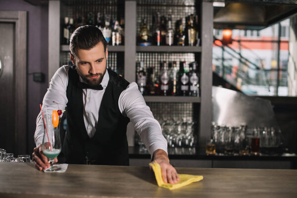 handsome young bartender cleaning bar counter with rag