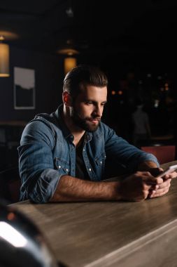 handsome man sitting at bar counter and using smartphone clipart