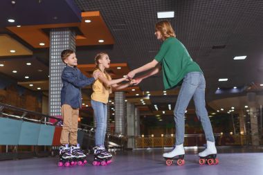 side view of mother and kids skating together on roller rink clipart