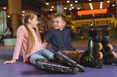 cute siblings in roller skates resting after skating on roller rink clipart