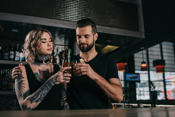 young bartenders clinking with drinks at bar