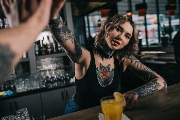 cropped image of tattooed bartender giving high five to visitor at bar