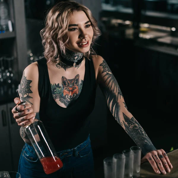 アルコールのボトルを押しながら離れて見て刺青のバーテンダー — ストック写真