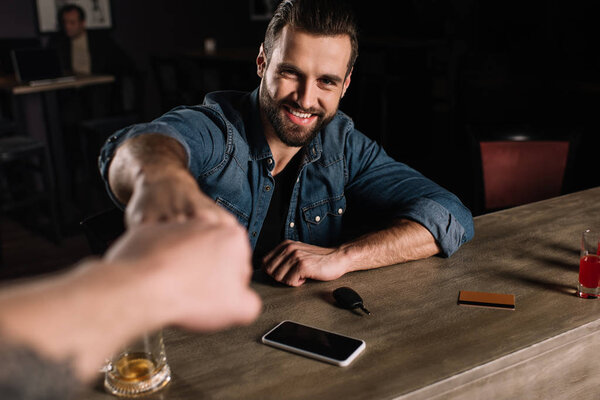 cropped image of visitor and bartender bumping fists at bar counter
