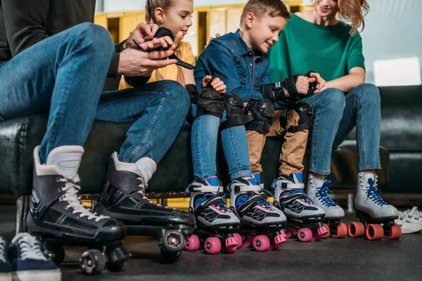 Vista parcial de los padres ayudando a los niños a usar protección antes de patinar en el parque de skate — Foto de Stock