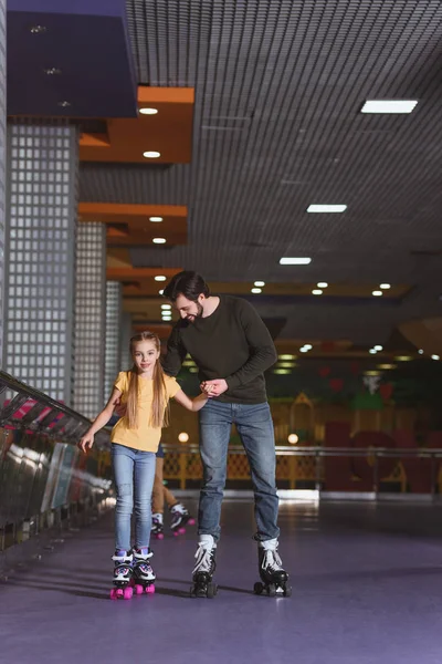 Father and daughter holding hands while skating together on roller rink — Stock Photo, Image