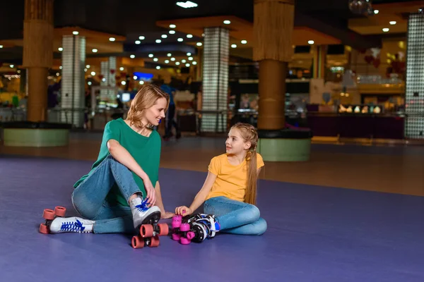 Mother and little daughter sitting on roller rink together — Stock Photo, Image