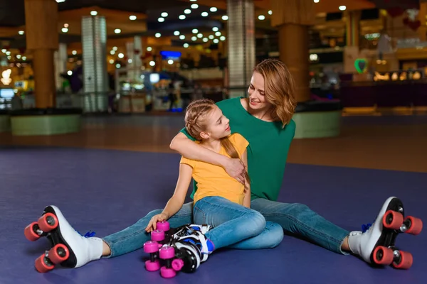 Smiling mother and little daughter sitting on roller rink together — Free Stock Photo