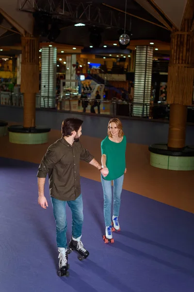 Young couple holding hands while skating together on roller rink — Free Stock Photo